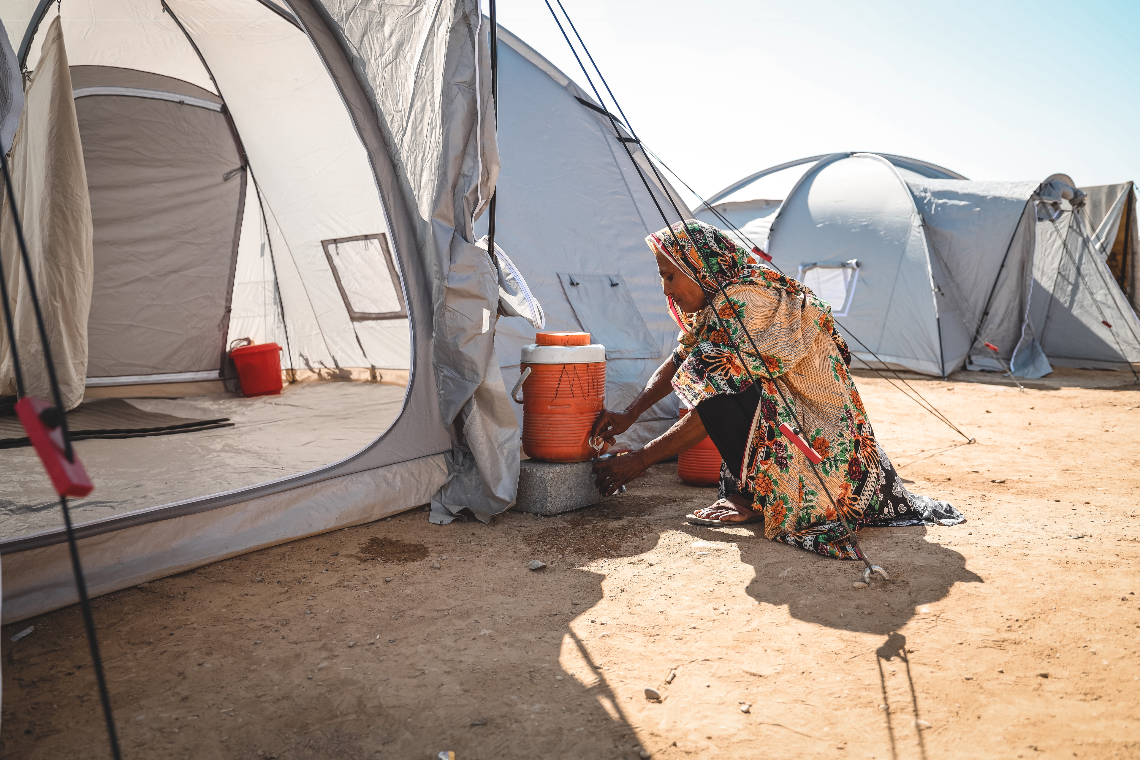 Woman washing her hands from a barrel at a tent. 