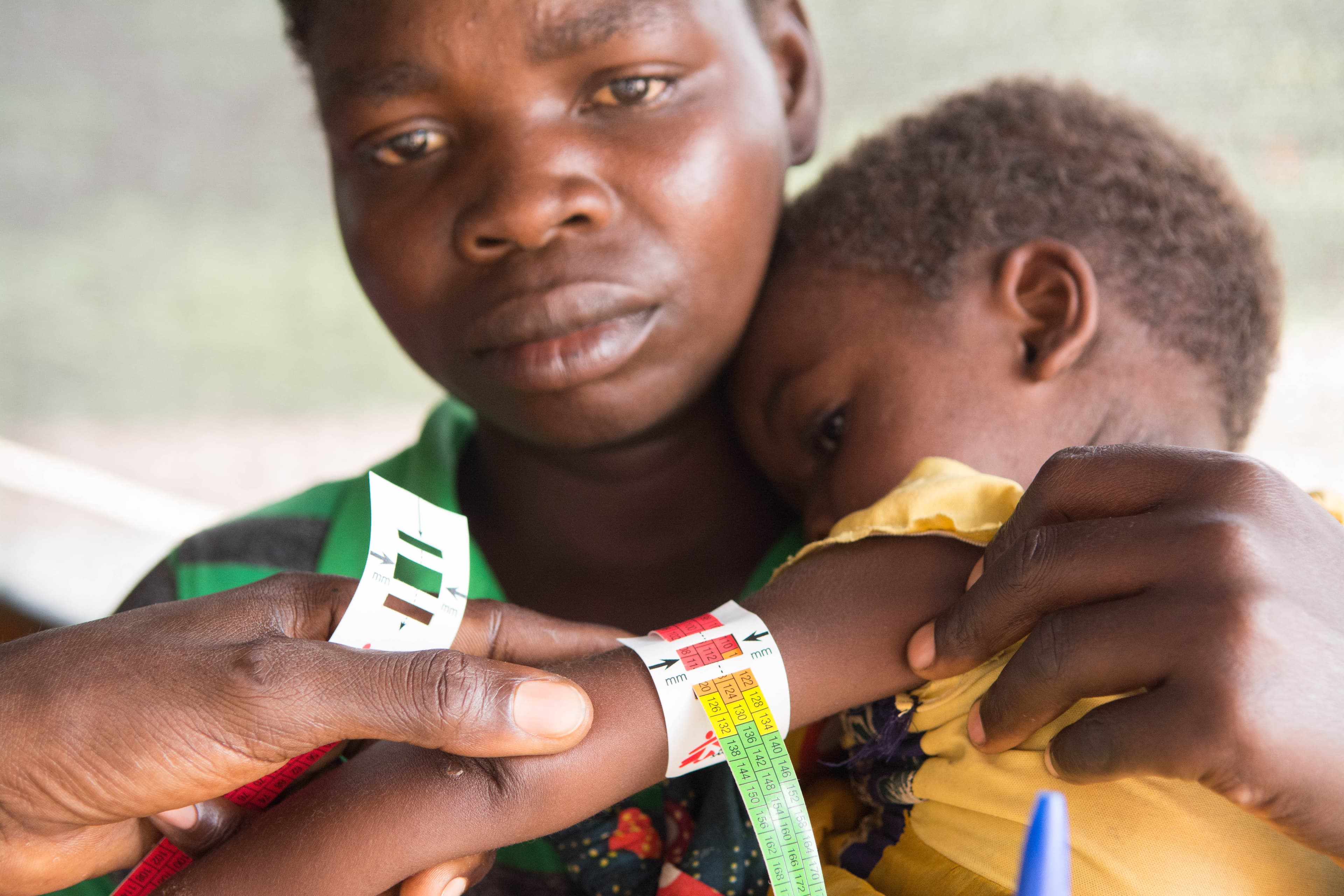 Woman holding a little baby while someone measures its upper arm circumference. 