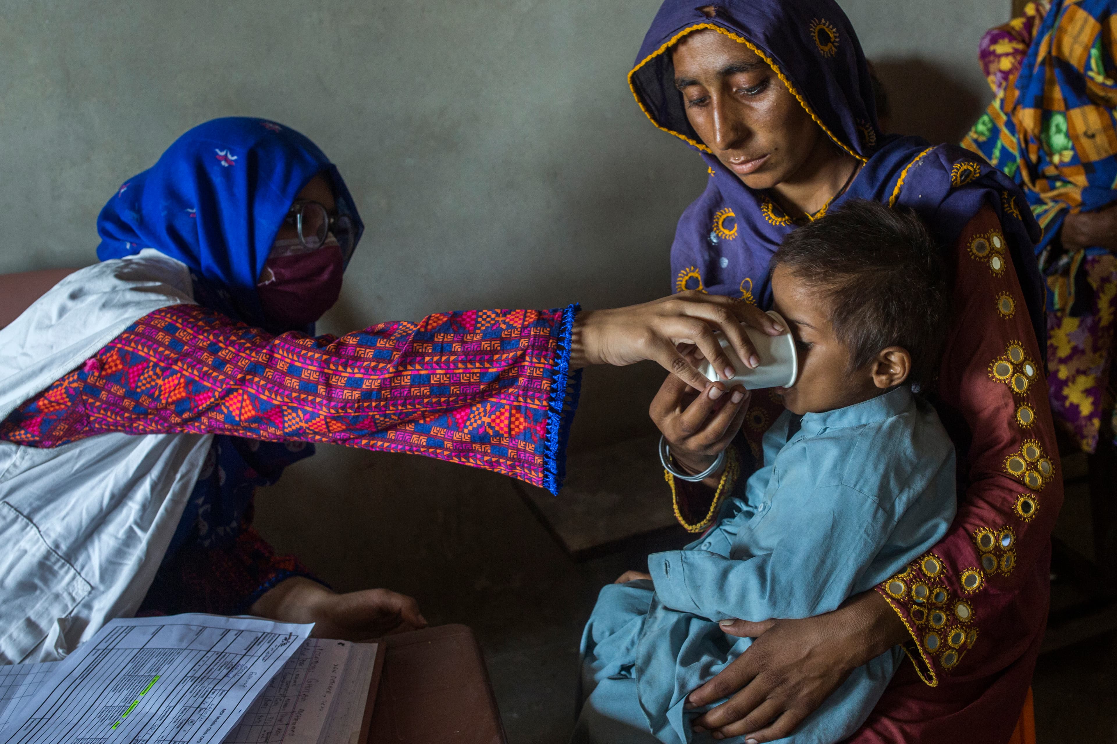 A woman stretching her arm to feed a child seated on a woman’s lap. 