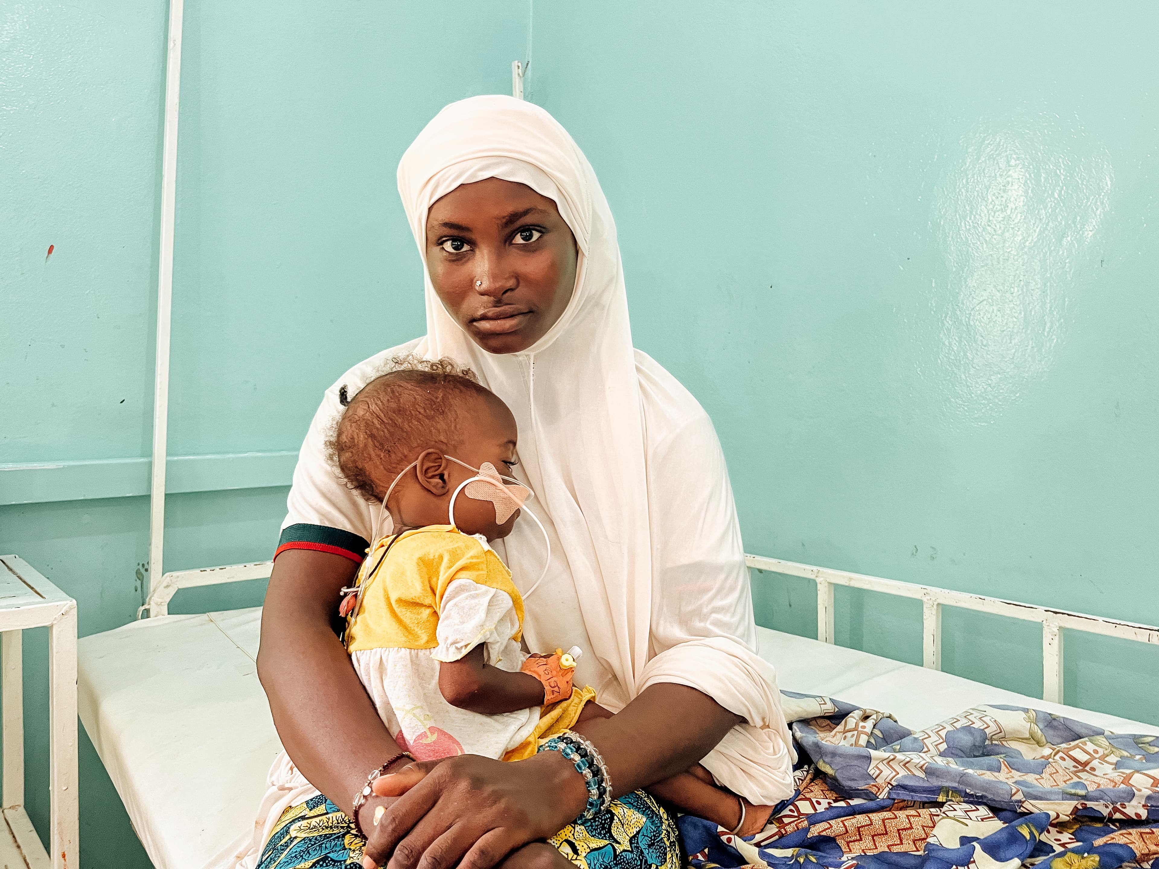 A woman holding a baby in her arms, while receiving medical treatment. 