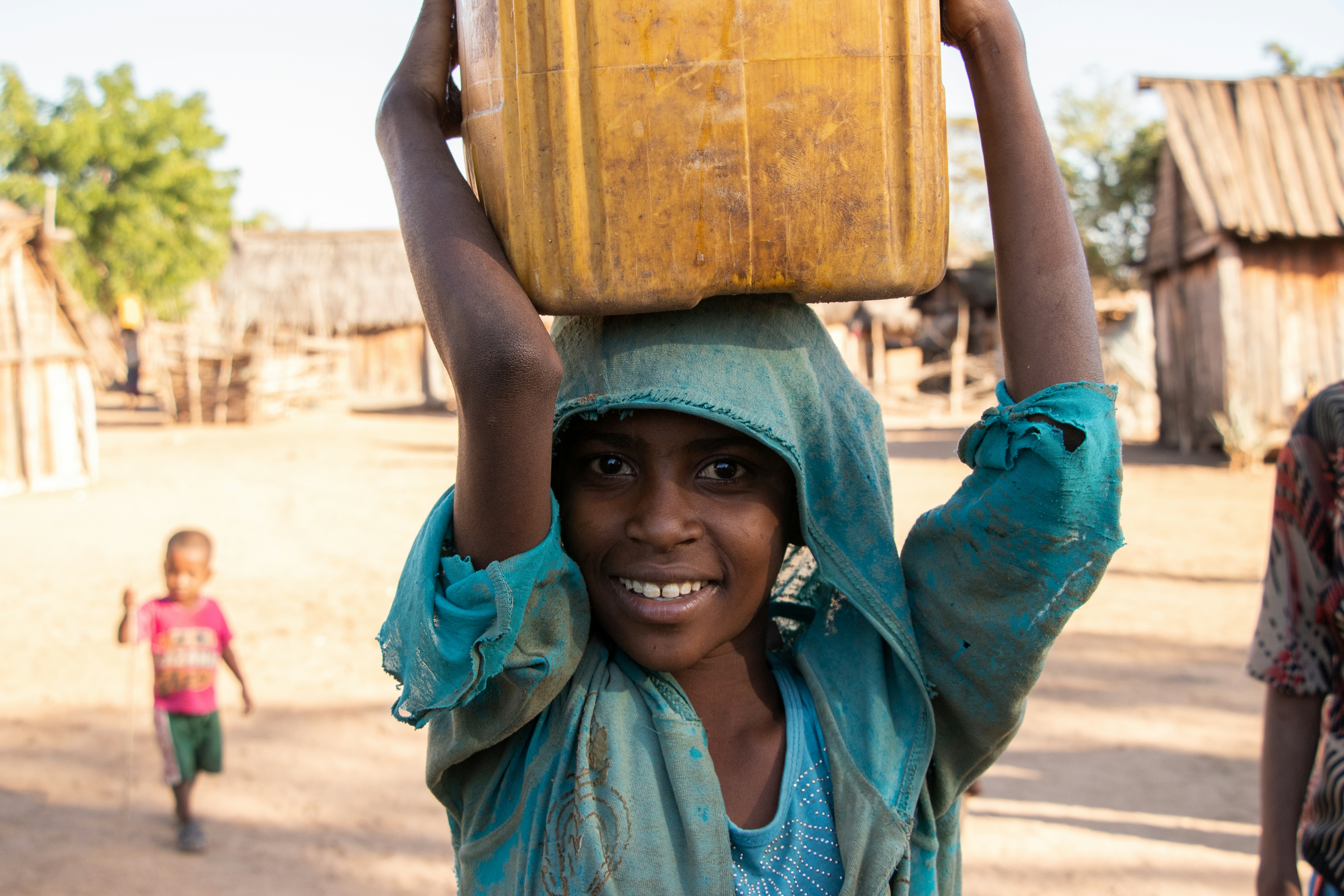 Portrait of a young African woman holding a yellow plastic barrel on her head. 