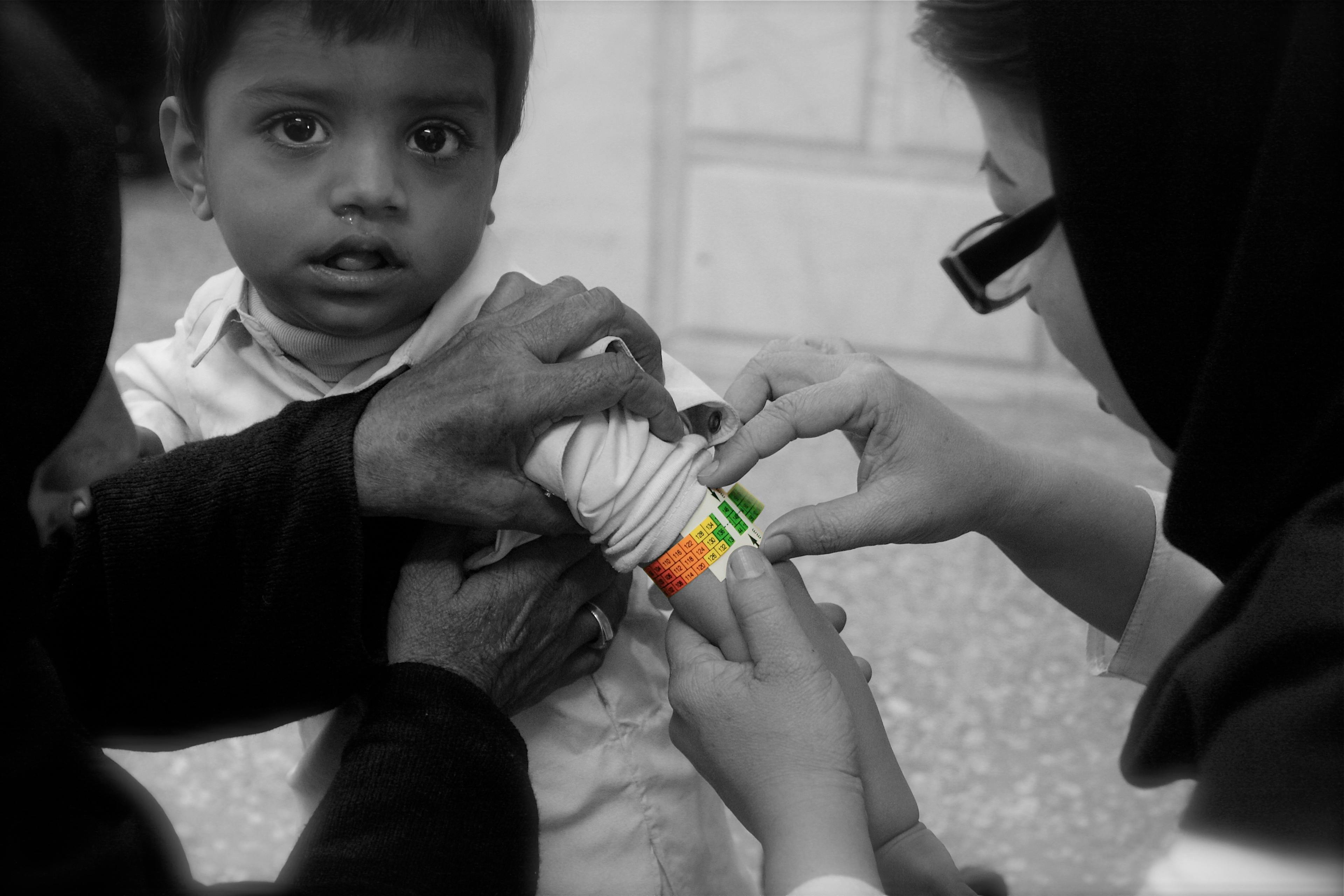 A child looking at camera while having hand measured by a medical staff. 