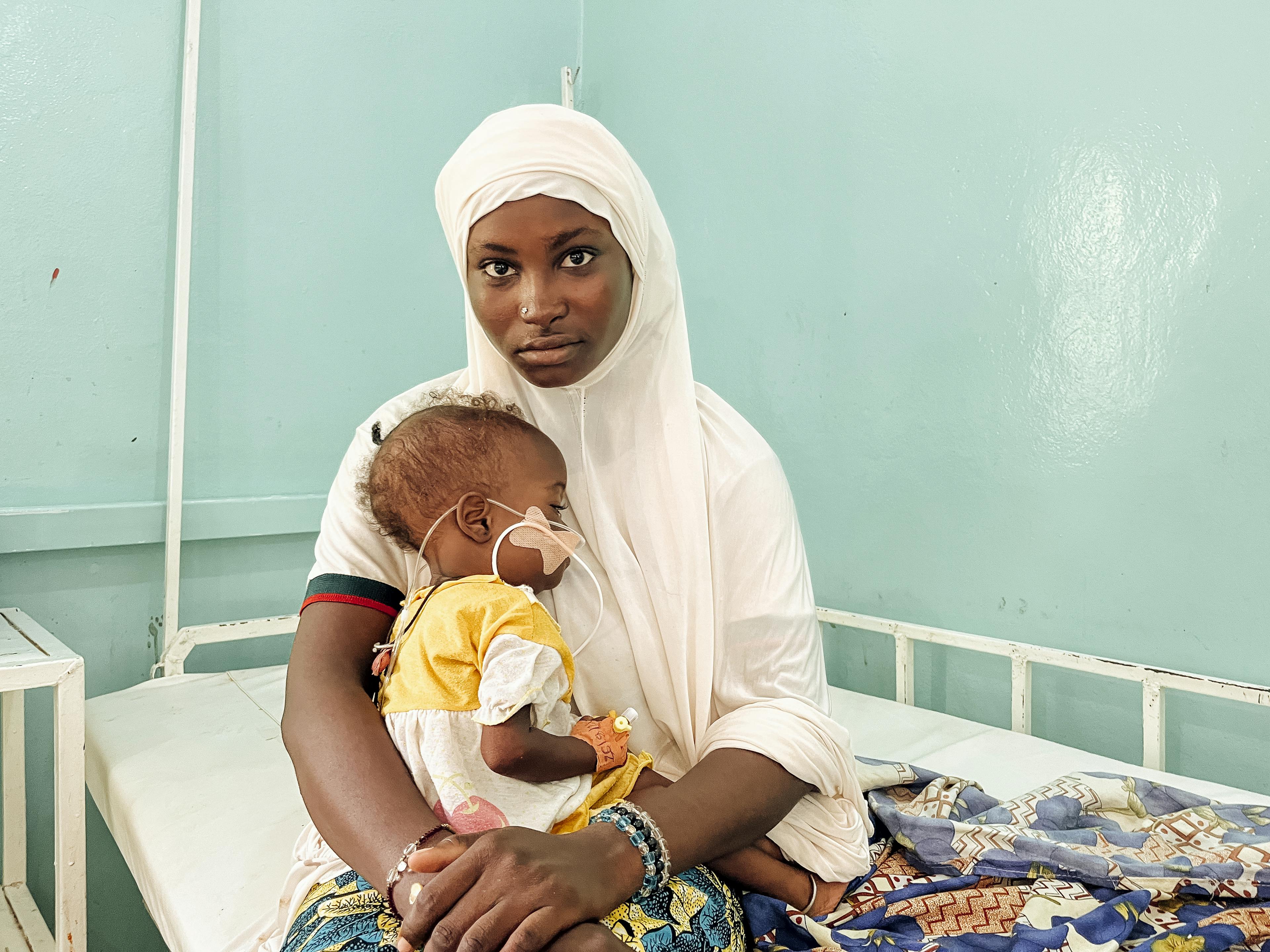 A woman holding a baby in her arms, while receiving medical treatment. 